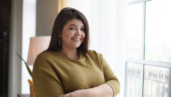 people-body-positivity-lifestyle-concept-indoor-image-adorable-overweight-chubby-young-lady-relaxing-home-standing-window-crossing-arms-her-chest-smiling-broadly